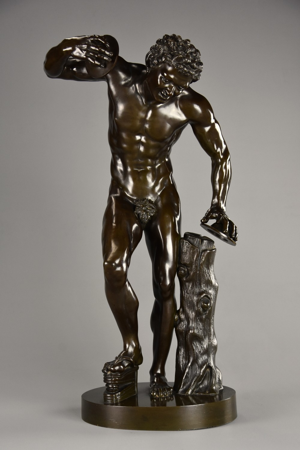 A late nineteenth-century dark brown patinated bronze sculpture depicting a nude dancing faun playing cymbals on a circular base.