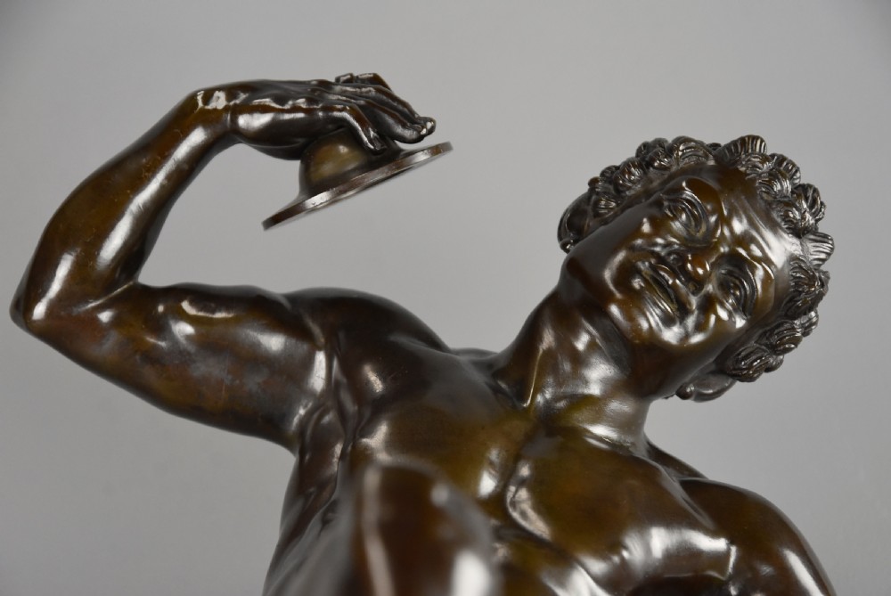 A late nineteenth-century dark brown patinated bronze sculpture depicting a nude dancing faun playing cymbals on a circular base. View VIII