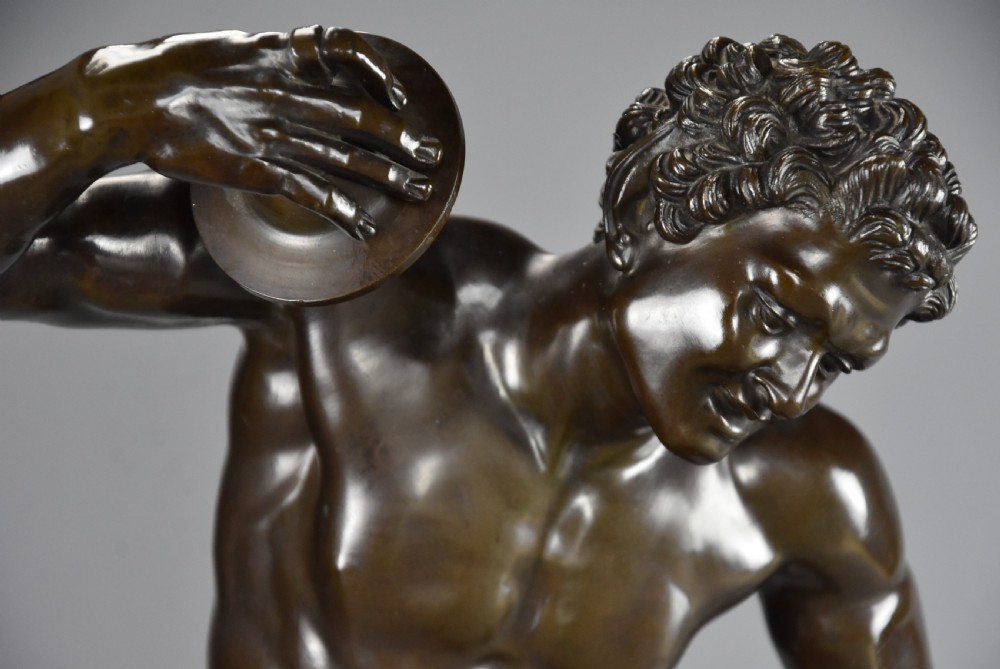 A late nineteenth-century dark brown patinated bronze sculpture depicting a nude dancing faun playing cymbals on a circular base. View IX