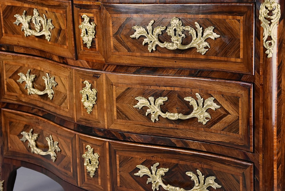 An 18th-century French Regence serpentine commode crafted in rosewood parquetry with gilded ormolu drawer pulls and a contoured marble top. View VIII