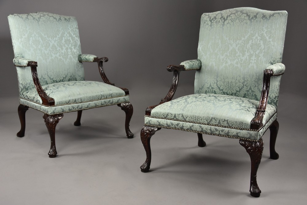 A pair of early 20th-century mahogany Gainsborough-style armchairs featuring carved cabriole legs with claw and ball feet, upholstered in light blue patterned damask fabric with brass stud trimming.