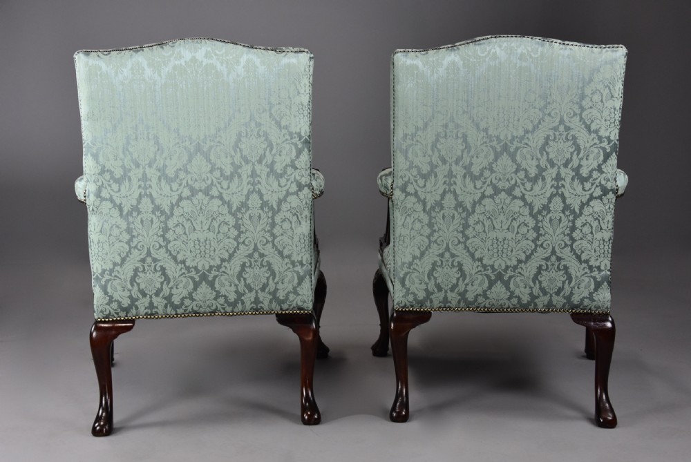 A pair of early 20th-century mahogany Gainsborough-style armchairs featuring carved cabriole legs with claw and ball feet, upholstered in light blue patterned damask fabric with brass stud trimming. View X