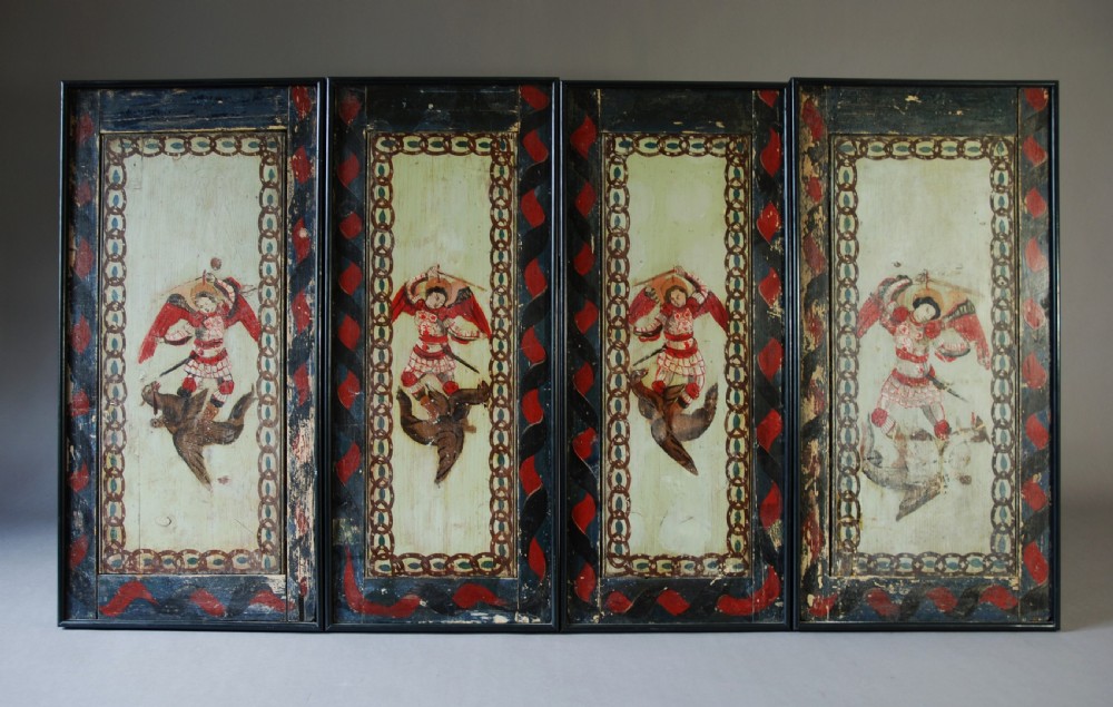 A set of four rectangular vertical pine panels decorated with naive paintings of Saint Michael slaying a winged dragon within chainlink borders.