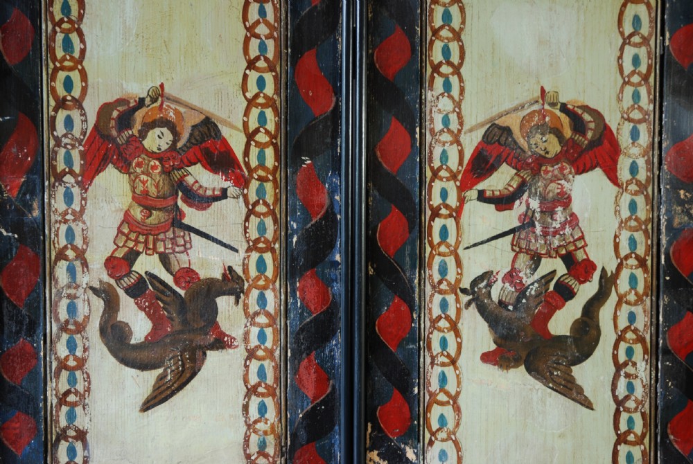 A set of four rectangular vertical pine panels decorated with naive paintings of Saint Michael slaying a winged dragon within chainlink borders. View V
