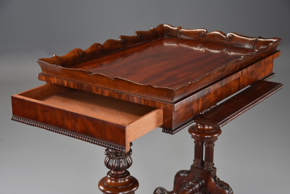 An early 19th century Regency mahogany work table featuring a wavy galleried tray top, flame mahogany apron with bead moulding, turned supports, and a carved stretcher base. View IX