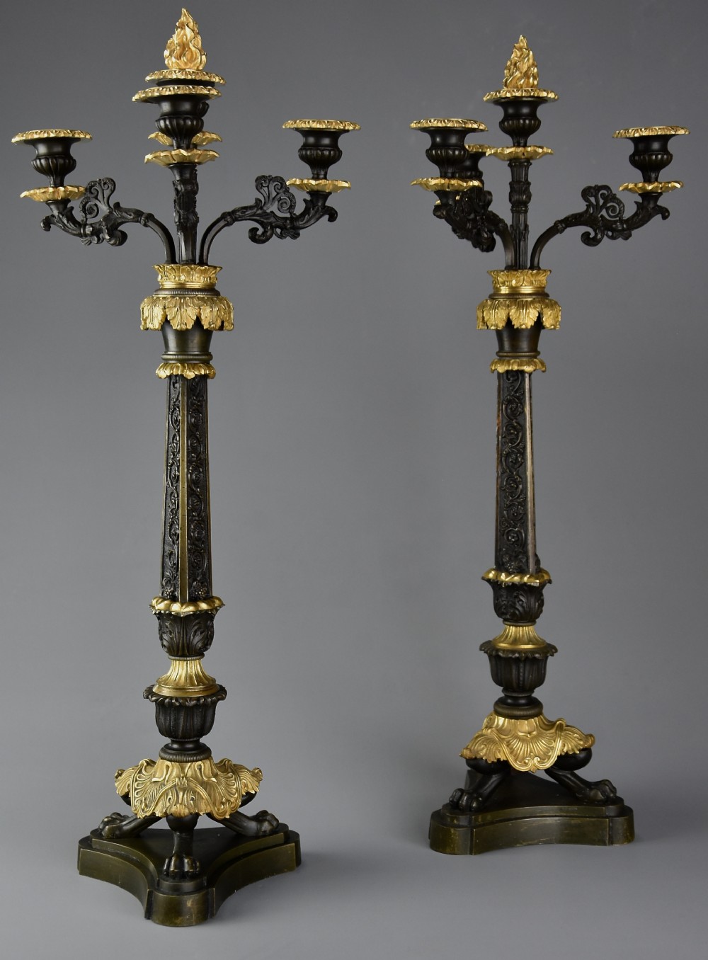 A pair of mid-19th century French Regence style candelabra crafted from patinated dark bronze with gilt bronze foliage mounts and three scrolled branches.