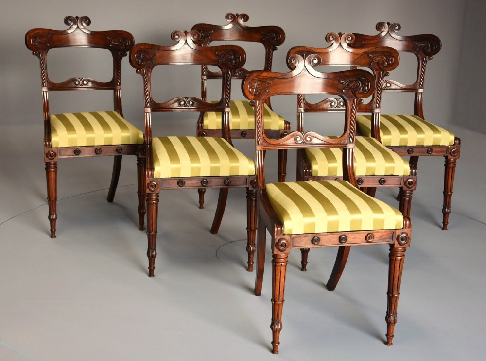 A set of six early nineteenth century Regency rosewood dining chairs with carved scroll crest rails and gold striped upholstered seats.
