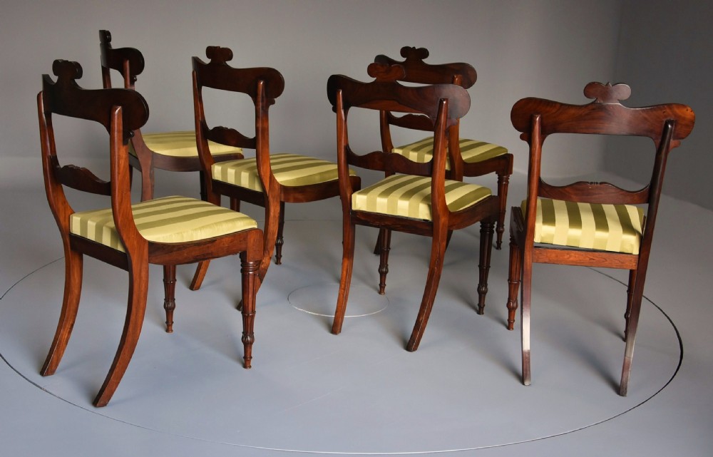 A set of six early nineteenth century Regency rosewood dining chairs with carved scroll crest rails and gold striped upholstered seats. View X