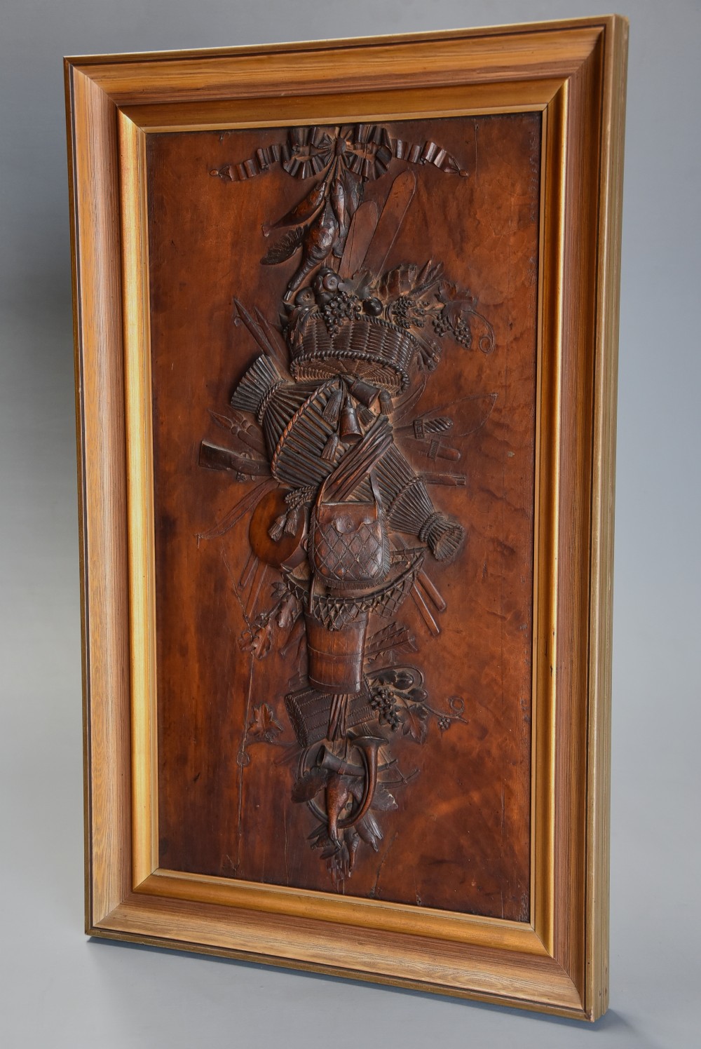 A framed mid-19th-century Continental fruitwood panel featuring a high-relief carved vertical trophy motif of hunting equipment, fruit, and foliage.
