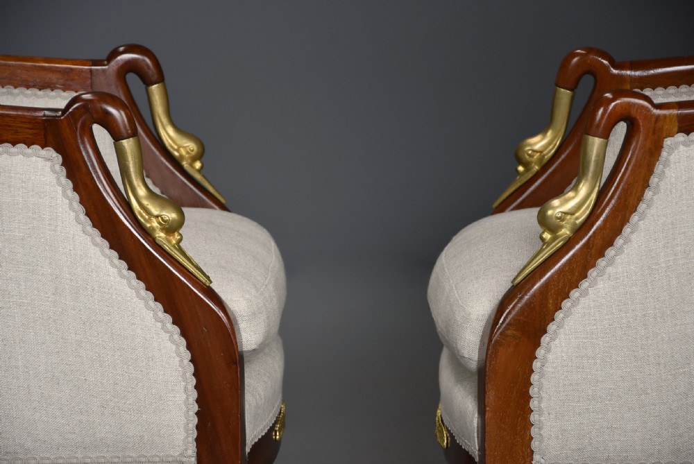 A pair of early 20th-century French Empire style mahogany armchairs featuring light neutral upholstery and gilt bronze mounts. View X