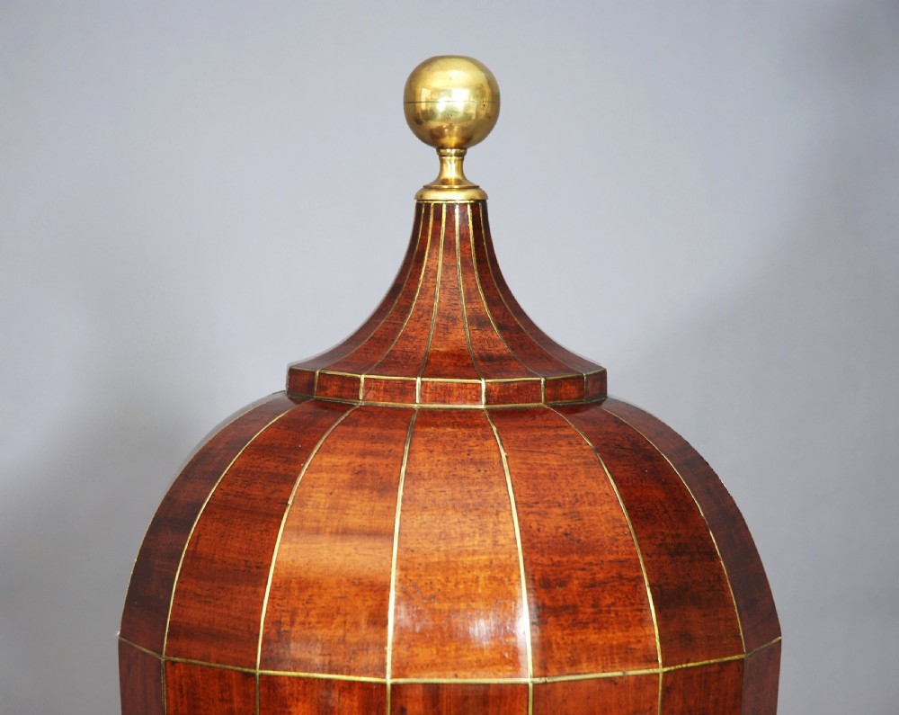 An 18th-century turned mahogany cutlery urn with brass stringing, lion mask ring handles, a top brass finial, and a stepped square base resting on brass ball feet. View IV