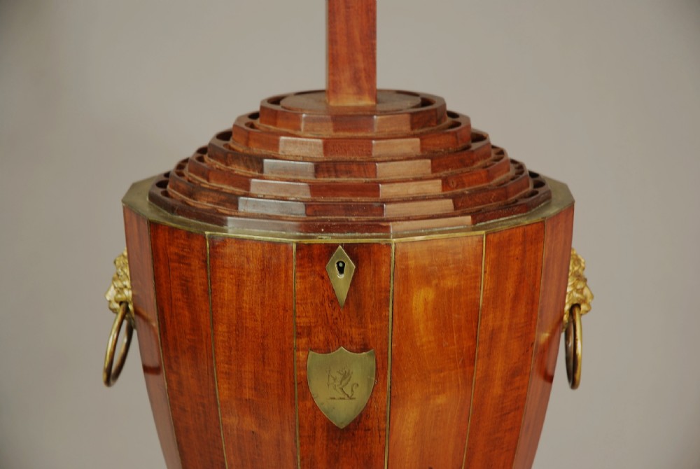 An 18th-century turned mahogany cutlery urn with brass stringing, lion mask ring handles, a top brass finial, and a stepped square base resting on brass ball feet. View V