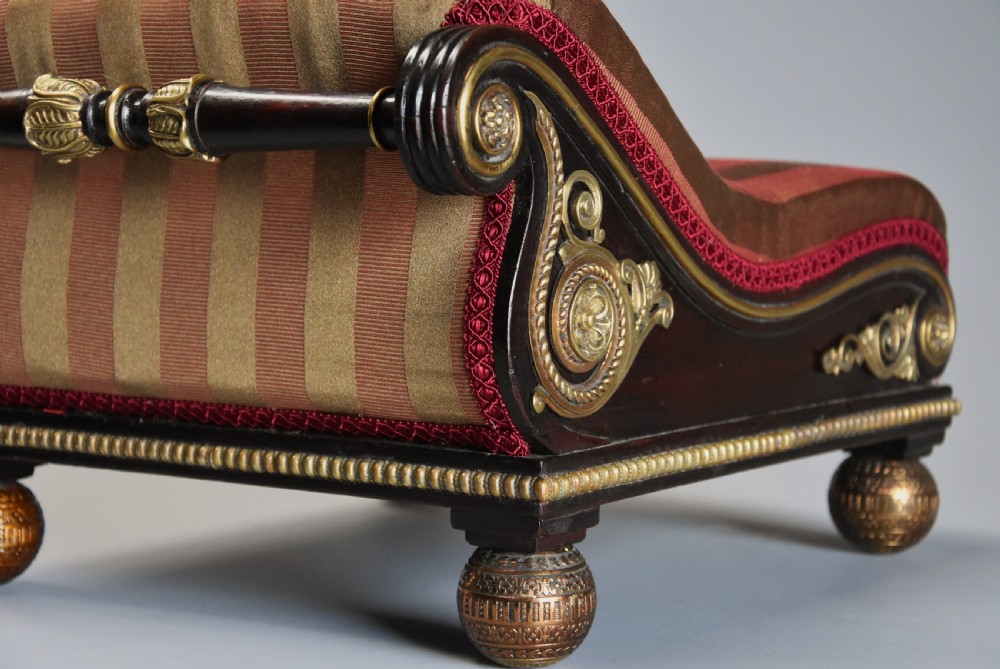 A nineteenth-century Regency mahogany footstool featuring a scrolled top upholstered in red and gold striped fabric with ornate gilt-metal mounts and ball feet. View III