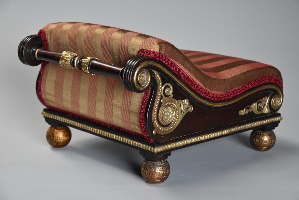 A nineteenth-century Regency mahogany footstool featuring a scrolled top upholstered in red and gold striped fabric with ornate gilt-metal mounts and ball feet. View IV