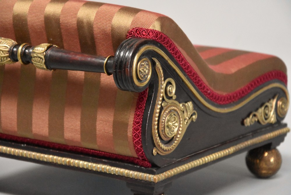 A nineteenth-century Regency mahogany footstool featuring a scrolled top upholstered in red and gold striped fabric with ornate gilt-metal mounts and ball feet. View V