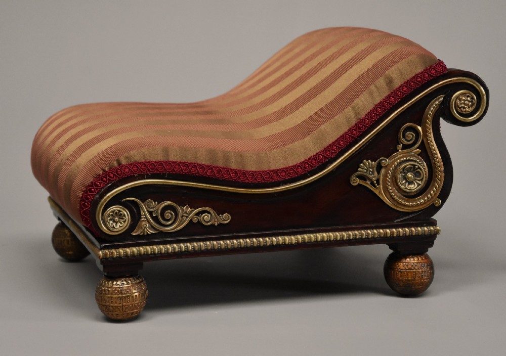 A nineteenth-century Regency mahogany footstool featuring a scrolled top upholstered in red and gold striped fabric with ornate gilt-metal mounts and ball feet. View VIII