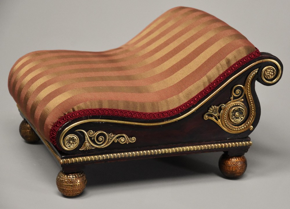 A nineteenth-century Regency mahogany footstool featuring a scrolled top upholstered in red and gold striped fabric with ornate gilt-metal mounts and ball feet. View IX