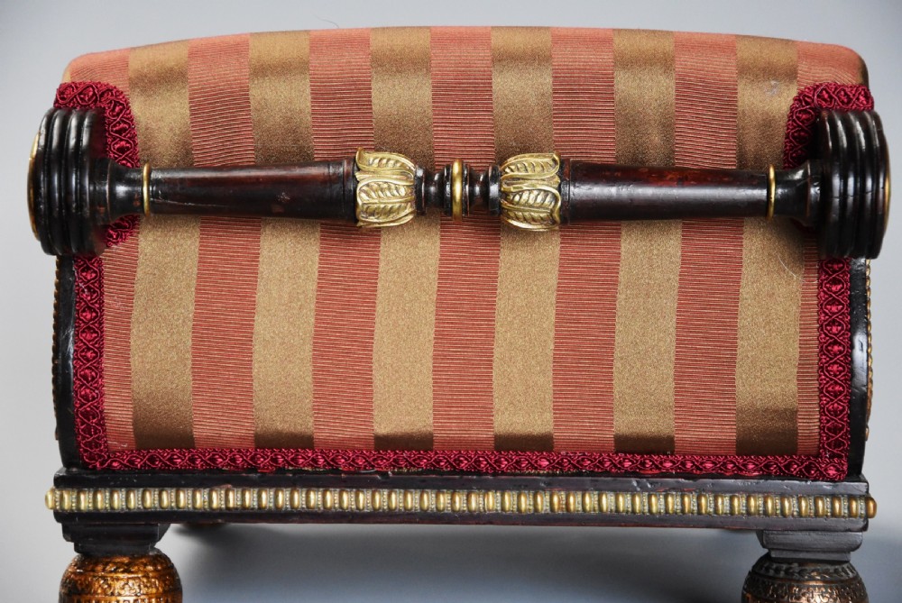 A nineteenth-century Regency mahogany footstool featuring a scrolled top upholstered in red and gold striped fabric with ornate gilt-metal mounts and ball feet. View XII
