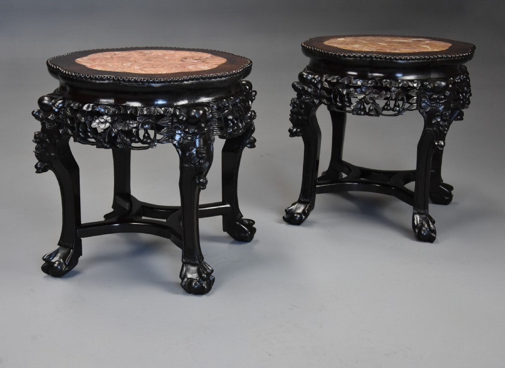 A pair of late nineteenth-century dark hardwood Chinese pot stands featuring carved foliage aprons, cabriole legs, and inset circular pink marble tops. View II