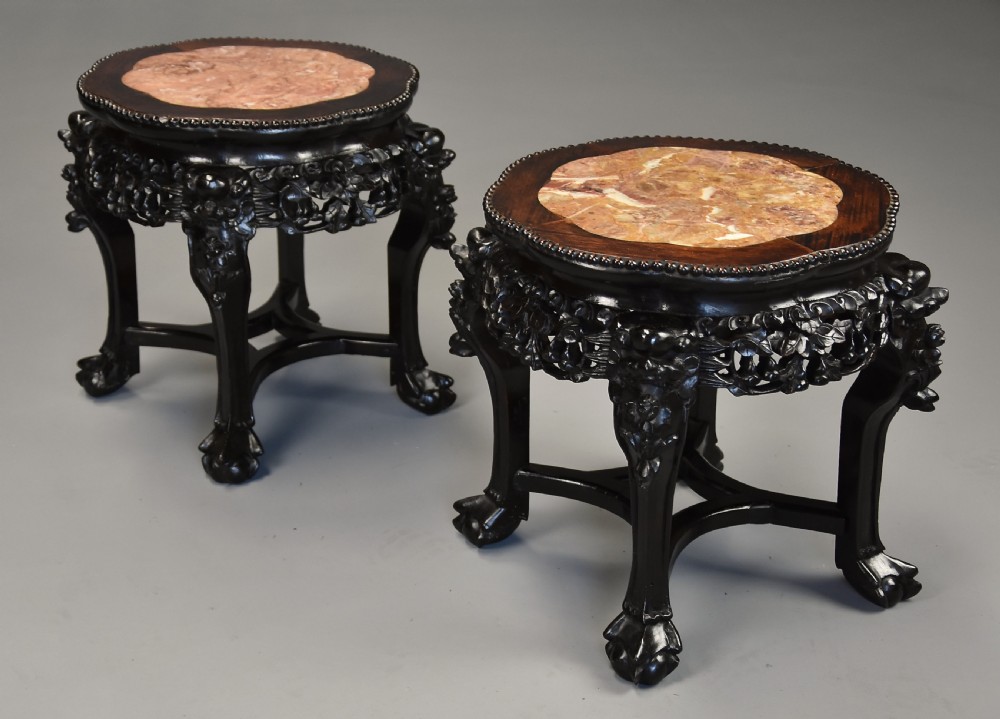 A pair of late nineteenth-century dark hardwood Chinese pot stands featuring carved foliage aprons, cabriole legs, and inset circular pink marble tops. View V