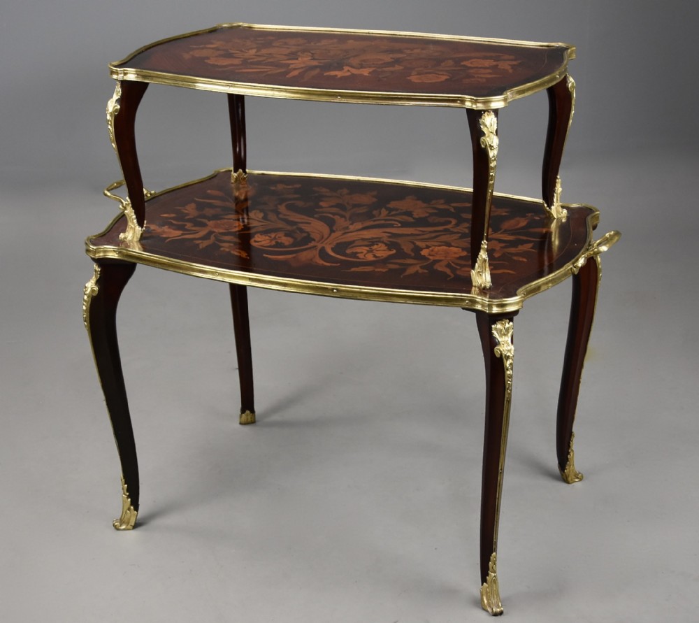 A two-tiered French style dark wood etagere featuring elaborate floral marquetry inlays, curved cabriole legs, and ornate gilt-bronze mounts along the rims and feet.