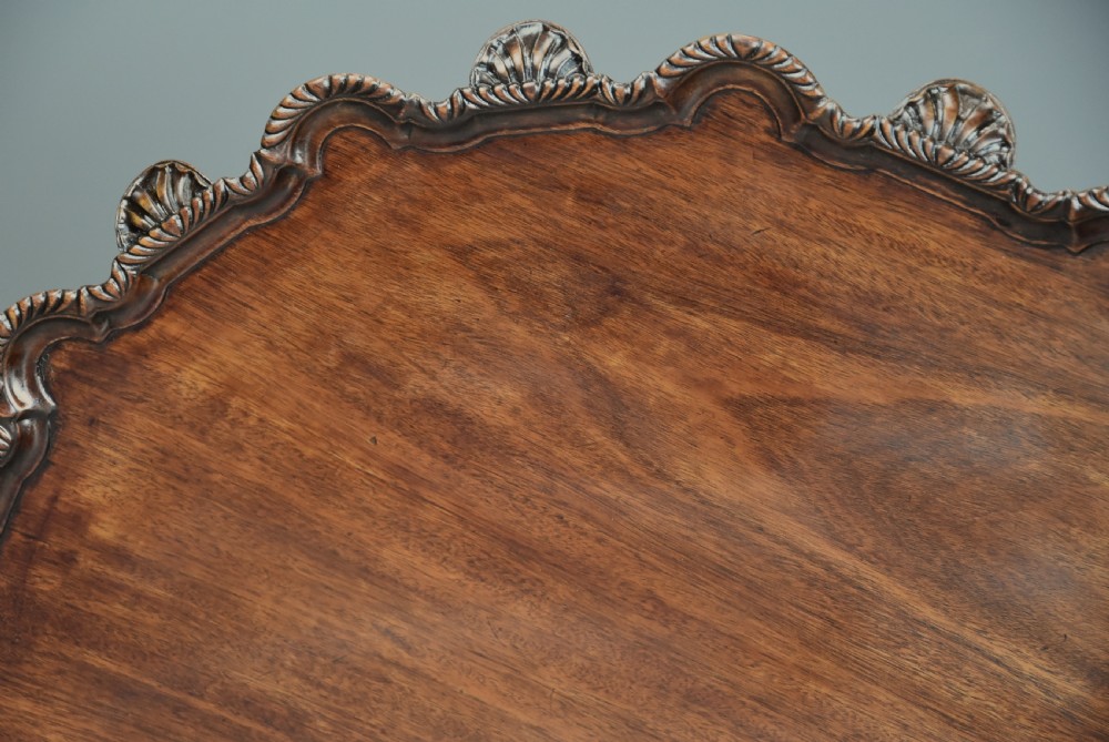 An early twentieth-century mahogany tilt-top tripod table with a carved piecrust border, turned column, and cabriole legs ending in claw-and-ball feet. View VII
