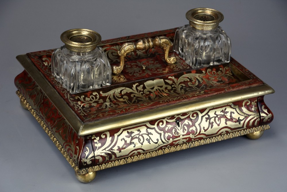 A mid-19th-century desk stand crafted with red tortoiseshell and brass scrollwork inlay, featuring two glass inkwells with brass lids, a central handle, and brass ball feet. View III