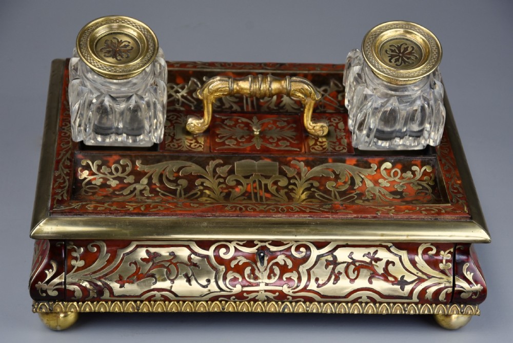 A mid-19th-century desk stand crafted with red tortoiseshell and brass scrollwork inlay, featuring two glass inkwells with brass lids, a central handle, and brass ball feet. View IV
