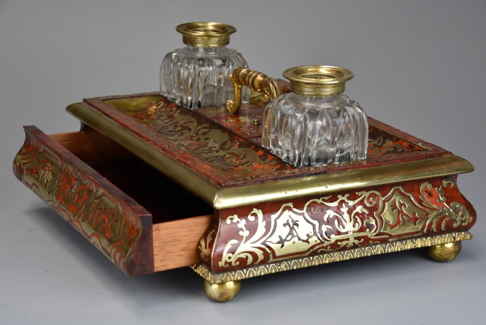 A mid-19th-century desk stand crafted with red tortoiseshell and brass scrollwork inlay, featuring two glass inkwells with brass lids, a central handle, and brass ball feet. View V