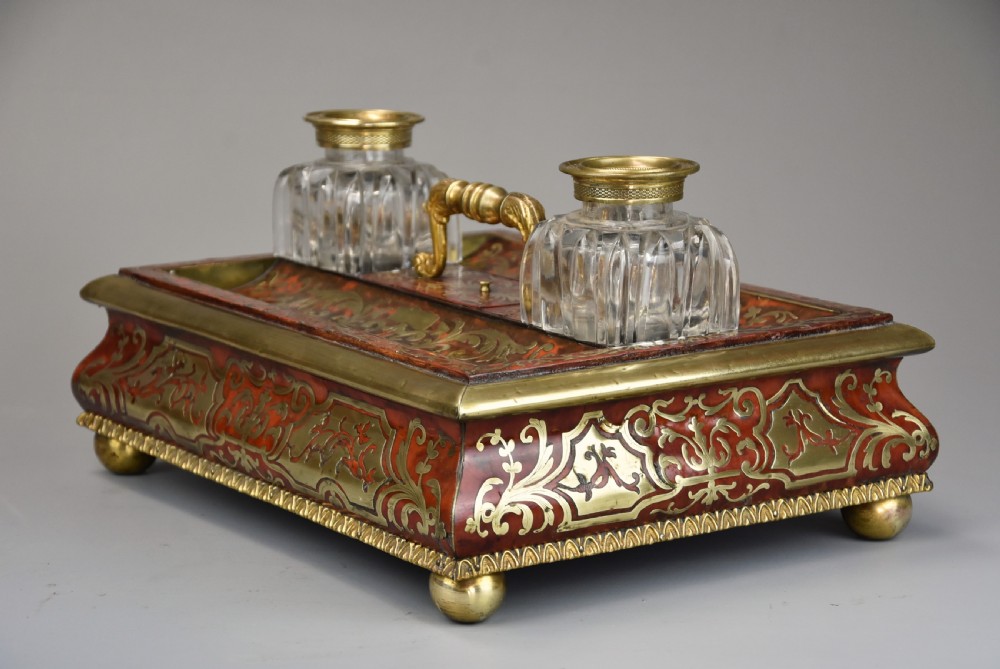 A mid-19th-century desk stand crafted with red tortoiseshell and brass scrollwork inlay, featuring two glass inkwells with brass lids, a central handle, and brass ball feet. View VII