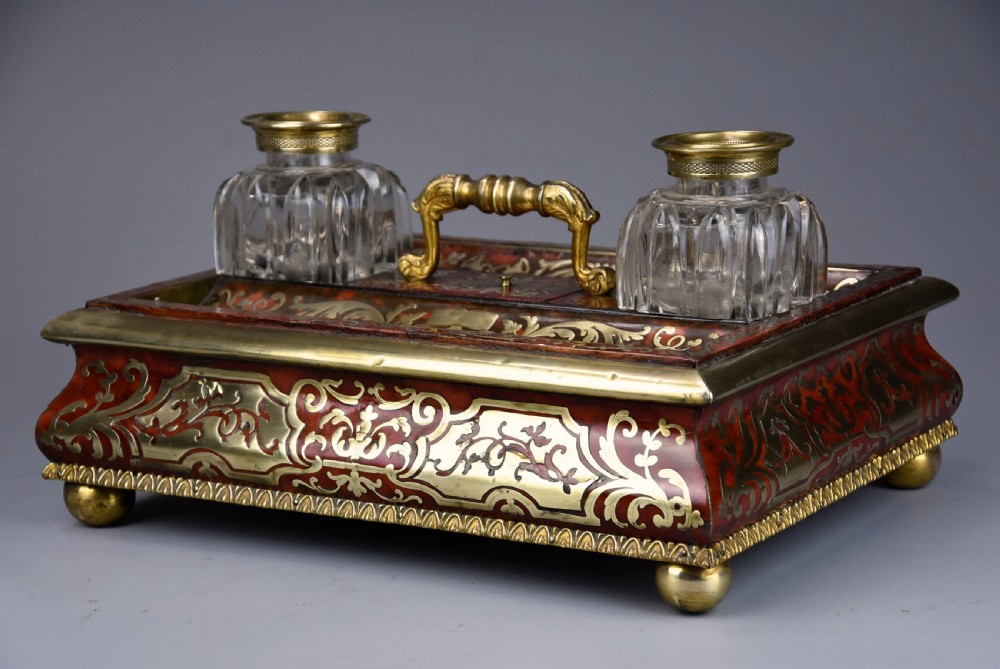 A mid-19th-century desk stand crafted with red tortoiseshell and brass scrollwork inlay, featuring two glass inkwells with brass lids, a central handle, and brass ball feet. View VIII