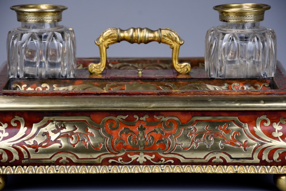 A mid-19th-century desk stand crafted with red tortoiseshell and brass scrollwork inlay, featuring two glass inkwells with brass lids, a central handle, and brass ball feet. View XI