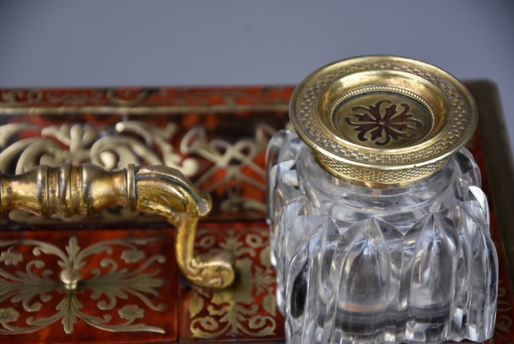 A mid-19th-century desk stand crafted with red tortoiseshell and brass scrollwork inlay, featuring two glass inkwells with brass lids, a central handle, and brass ball feet. View XII