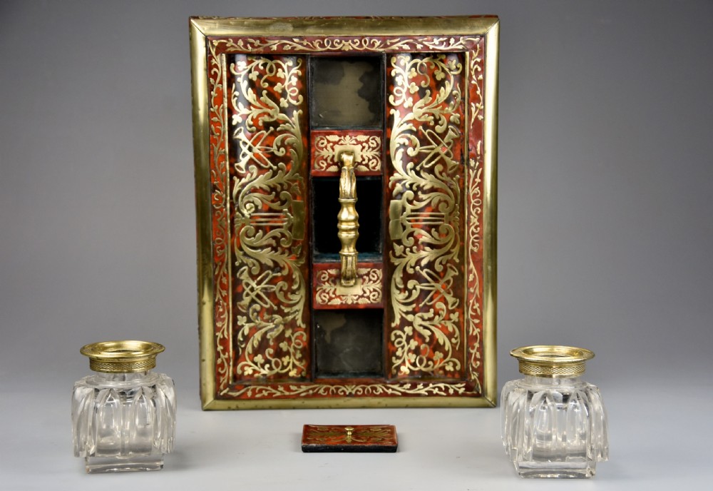 A mid-19th-century desk stand crafted with red tortoiseshell and brass scrollwork inlay, featuring two glass inkwells with brass lids, a central handle, and brass ball feet. View XIII