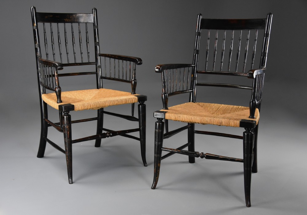 A pair of late nineteenth-century ebonised wooden armchairs featuring turned spindle backrests, woven rush seats, and turned legs with stretchers.
