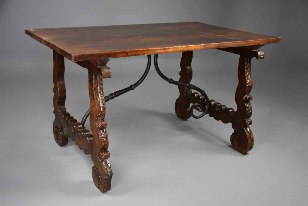 A solid walnut trestle table featuring carved decorative legs, hand-forged wrought iron stretchers, and a dark polished top. View II
