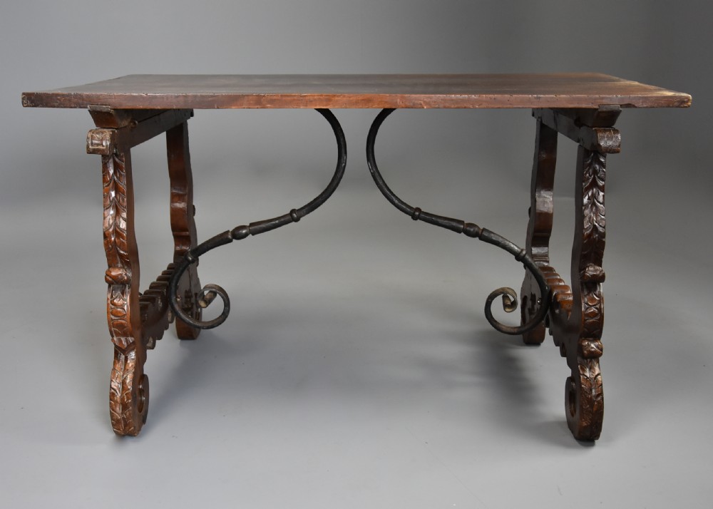 A solid walnut trestle table featuring carved decorative legs, hand-forged wrought iron stretchers, and a dark polished top. View III