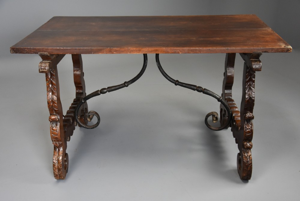 A solid walnut trestle table featuring carved decorative legs, hand-forged wrought iron stretchers, and a dark polished top. View IV