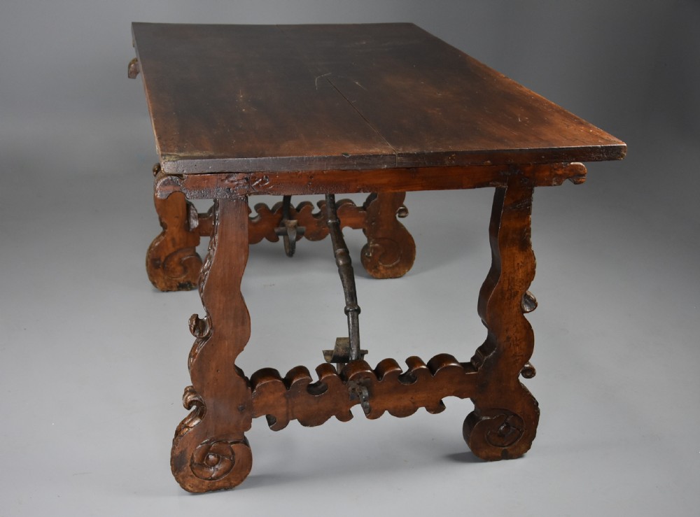 A solid walnut trestle table featuring carved decorative legs, hand-forged wrought iron stretchers, and a dark polished top. View VIII