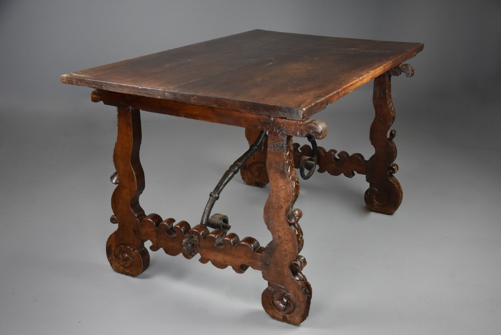 A solid walnut trestle table featuring carved decorative legs, hand-forged wrought iron stretchers, and a dark polished top. View XI