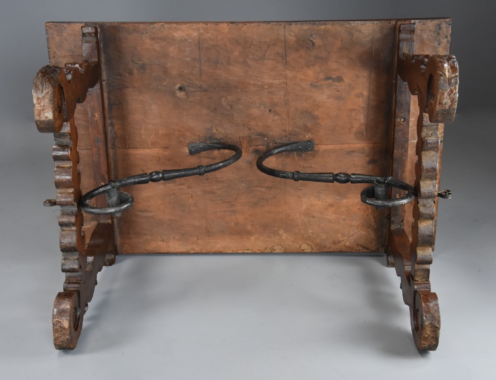 A solid walnut trestle table featuring carved decorative legs, hand-forged wrought iron stretchers, and a dark polished top. View XIV
