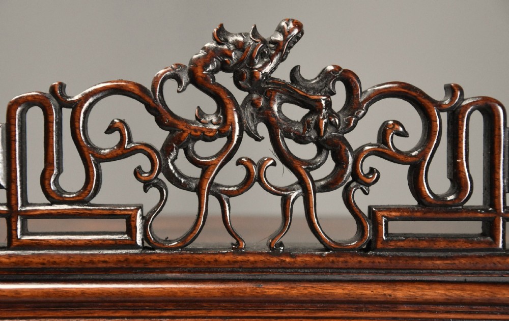A late 19th-century dark padouk display cabinet featuring asymmetrical shelving, reticulated fretwork, and inlaid pictorial panel doors. View VI
