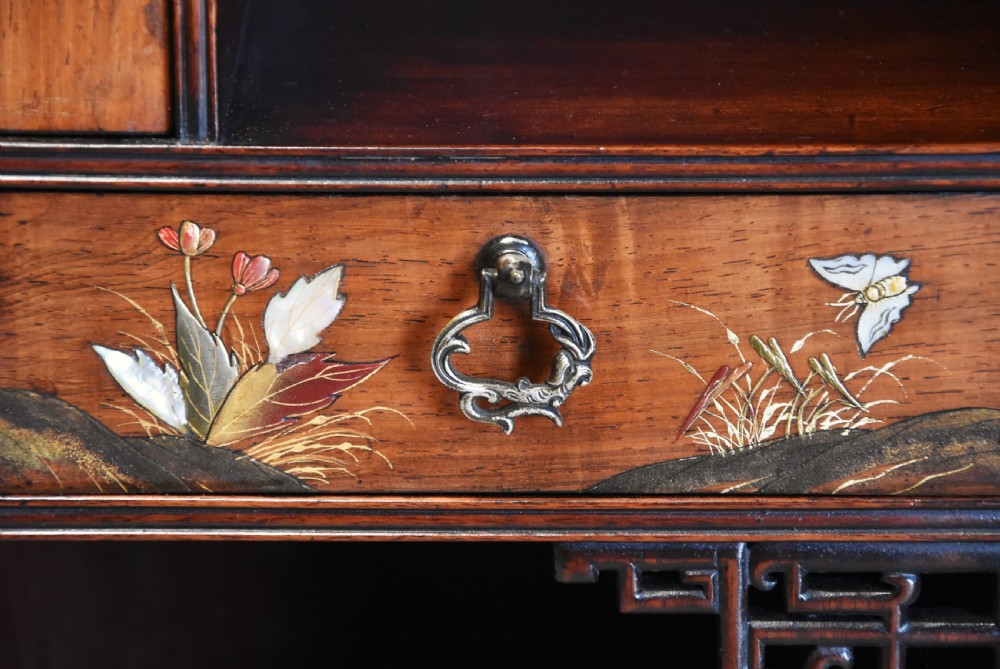 A late 19th-century dark padouk display cabinet featuring asymmetrical shelving, reticulated fretwork, and inlaid pictorial panel doors. View XII