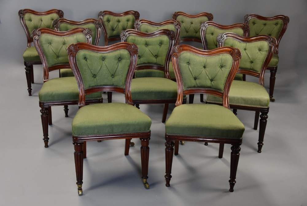 A matched set of twelve mid-19th century William IV mahogany dining chairs featuring buttoned green upholstered backrests and turned fluted front legs on brass castors.