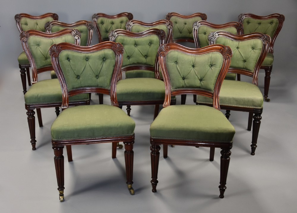 A matched set of twelve mid-19th century William IV mahogany dining chairs featuring buttoned green upholstered backrests and turned fluted front legs on brass castors. View II