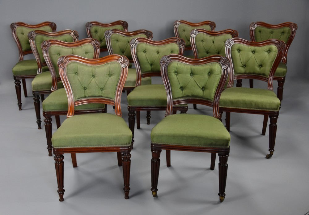 A matched set of twelve mid-19th century William IV mahogany dining chairs featuring buttoned green upholstered backrests and turned fluted front legs on brass castors. View IV