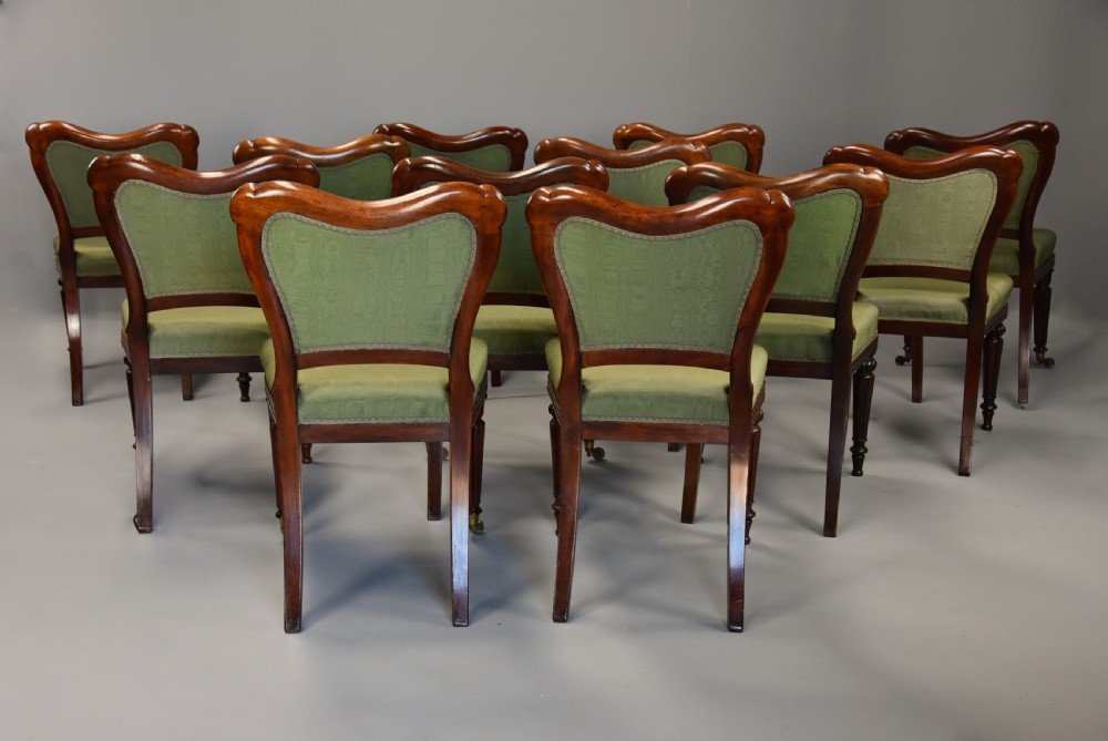 A matched set of twelve mid-19th century William IV mahogany dining chairs featuring buttoned green upholstered backrests and turned fluted front legs on brass castors. View XIII