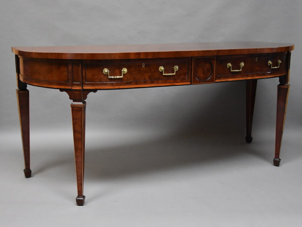 A late 18th-century Sheraton mahogany bowfront side table with two drawers, brass swan-neck handles, boxwood inlay, and square tapered legs.