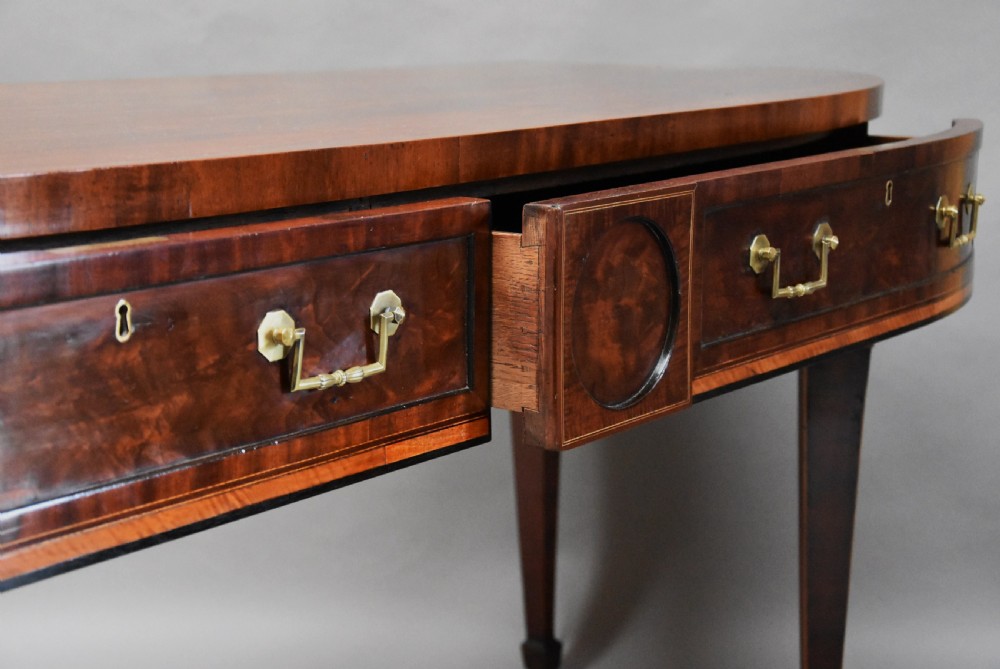 A late 18th-century Sheraton mahogany bowfront side table with two drawers, brass swan-neck handles, boxwood inlay, and square tapered legs. View X