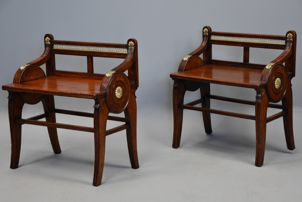 A pair of late nineteenth-century dark oak hall benches featuring carved side roundels, brass mounts, and a spindle gallery back.